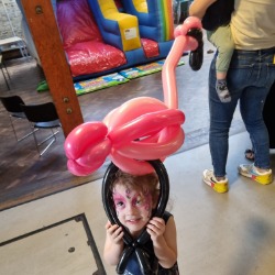 Girl with flamingo facepaint holdng a flamingo balloon at an indoor party in London
