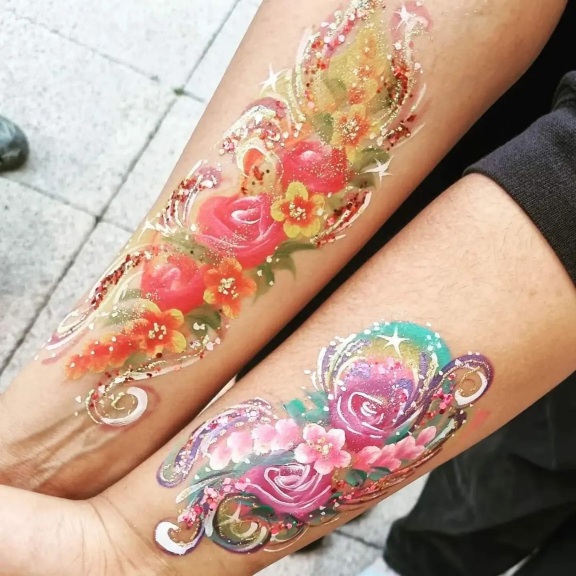 Face paint on the arms of two people, intricate flower designs with glitter